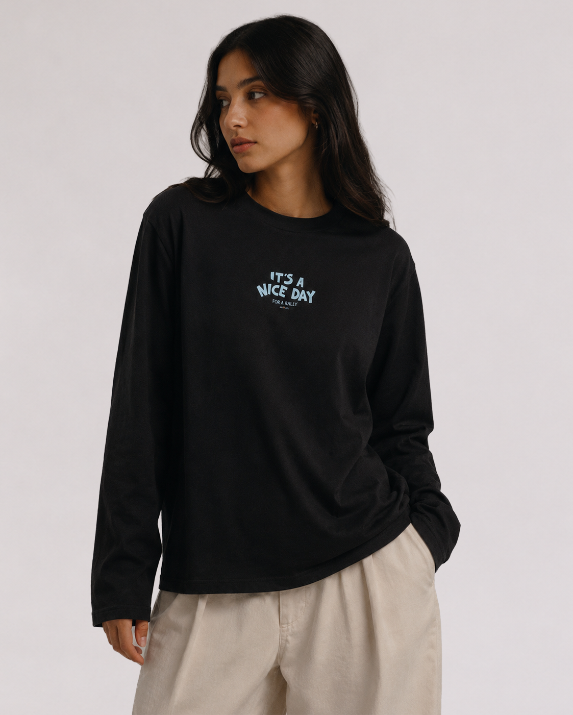 Woman wearing Third Shot black long-sleeve tee with pale blue "It's a Nice Day For a Rally" chest print, styled with cream trousers