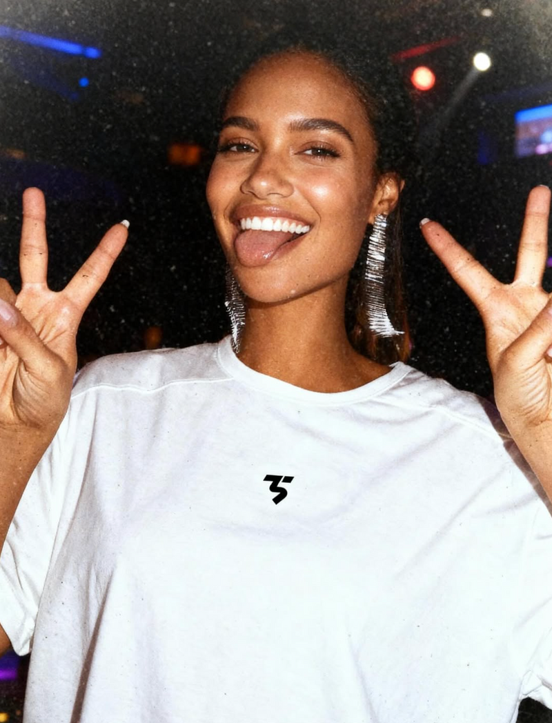 Person wearing a white t-shirt with a logo, making peace signs with both hands.